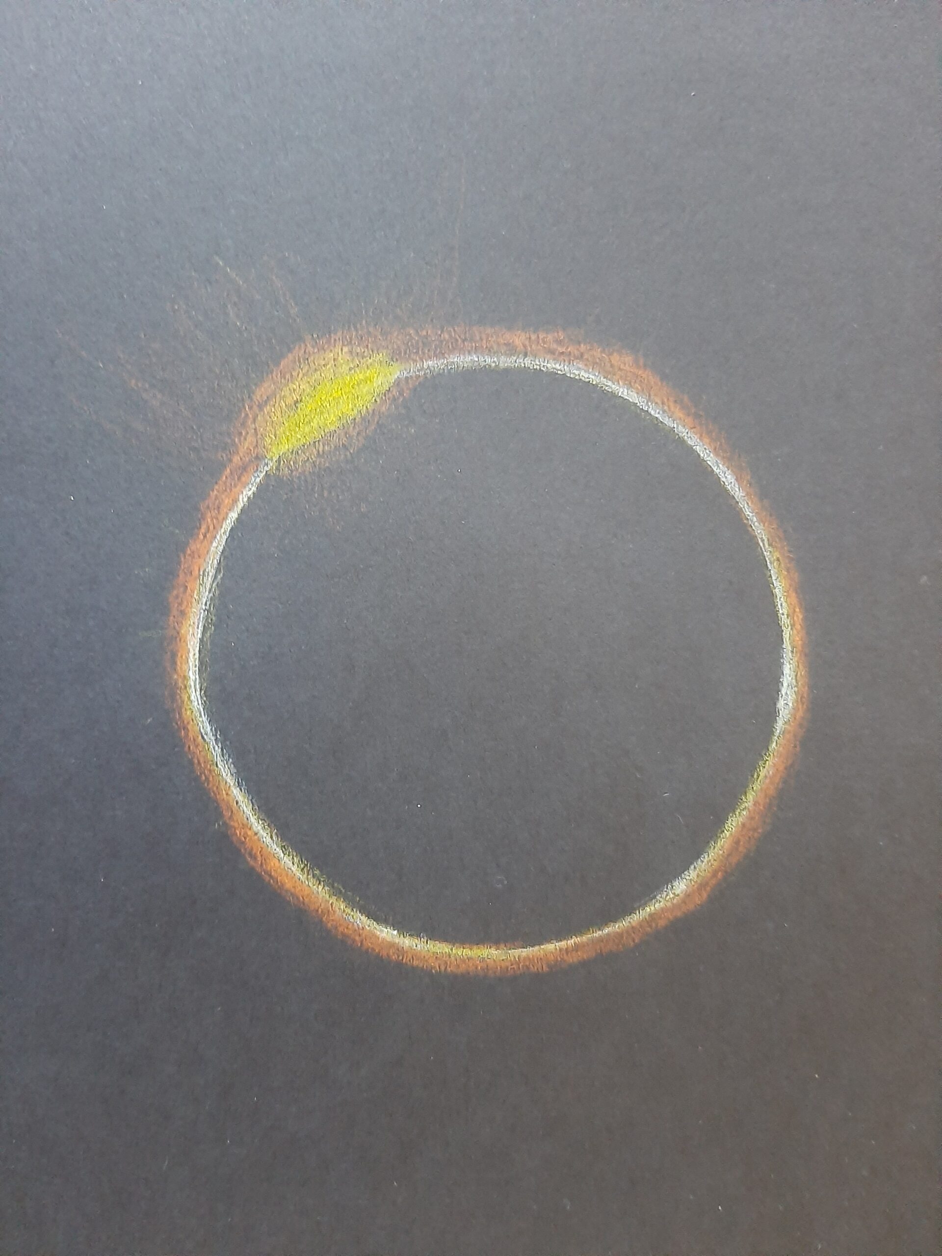 Black circle with a yellow and orange glow around it and one brighter yellow spot in the top