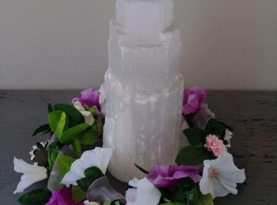 A tower of selenite crystal surrounded by a flower garland