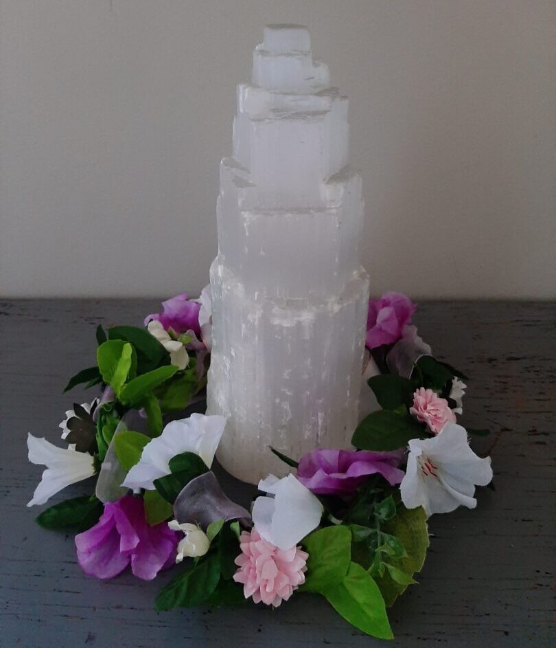 A tower of selenite crystal surrounded by a flower garland
