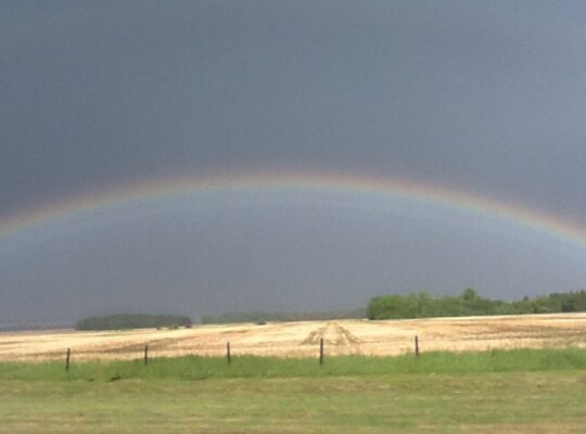 Rainbow beneath dark summer clouds over a harvested field at Lammas
