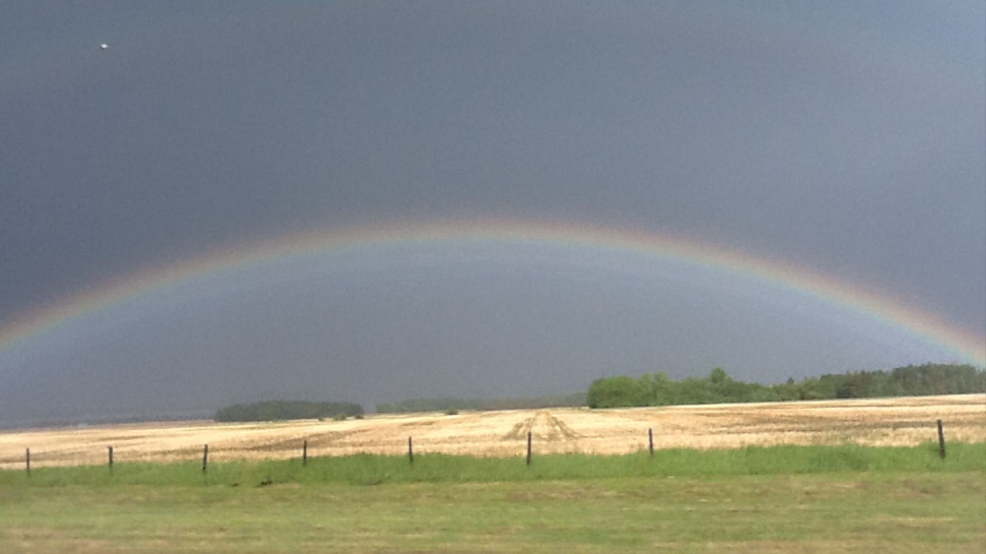 Rainbow beneath dark summer clouds over a harvested field at Lammas